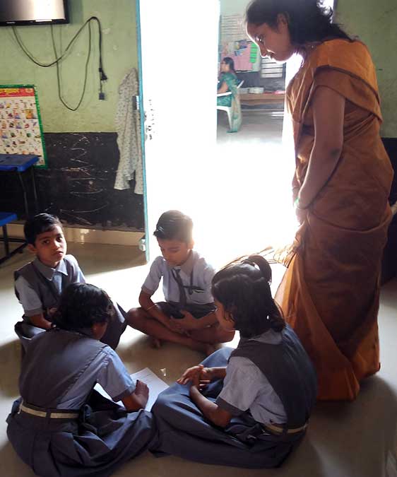 विद्यार्थी गट चर्चा करत असताना मदत करताना शिक्षिका